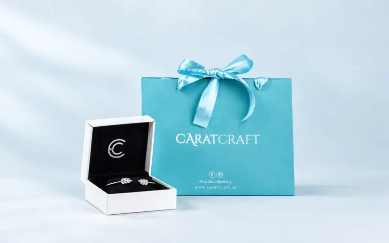Carat Craft jewelry box with a bracelet beside a turquoise gift bag tied with a satin bow