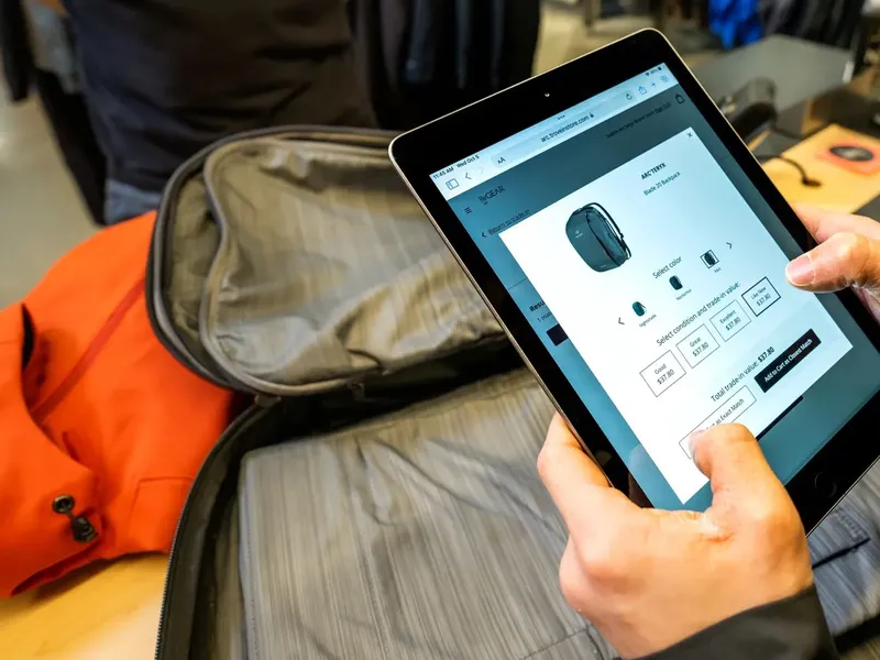 Hand holding a tablet showing a resale trade-in evaluation for a backpack