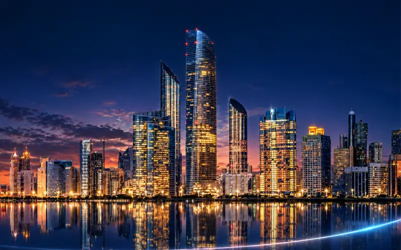 City skyline at night with glowing high-rise towers reflected in the water