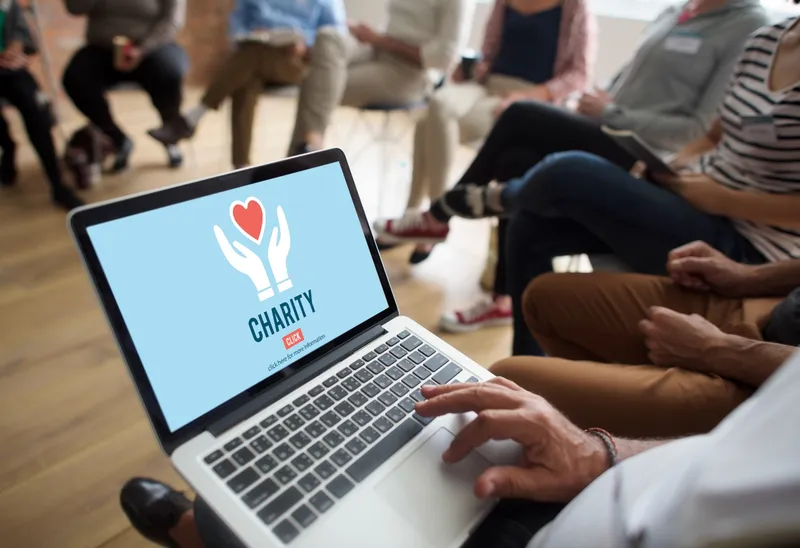 Laptop displaying a charity donation graphic, with people seated in the background